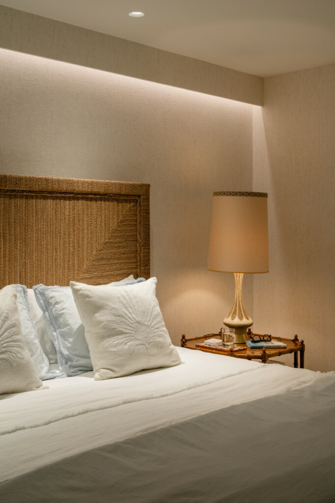 Elegant bedroom featuring textured wallpaper, ambient cove lighting, woven headboard, and brass table lamp