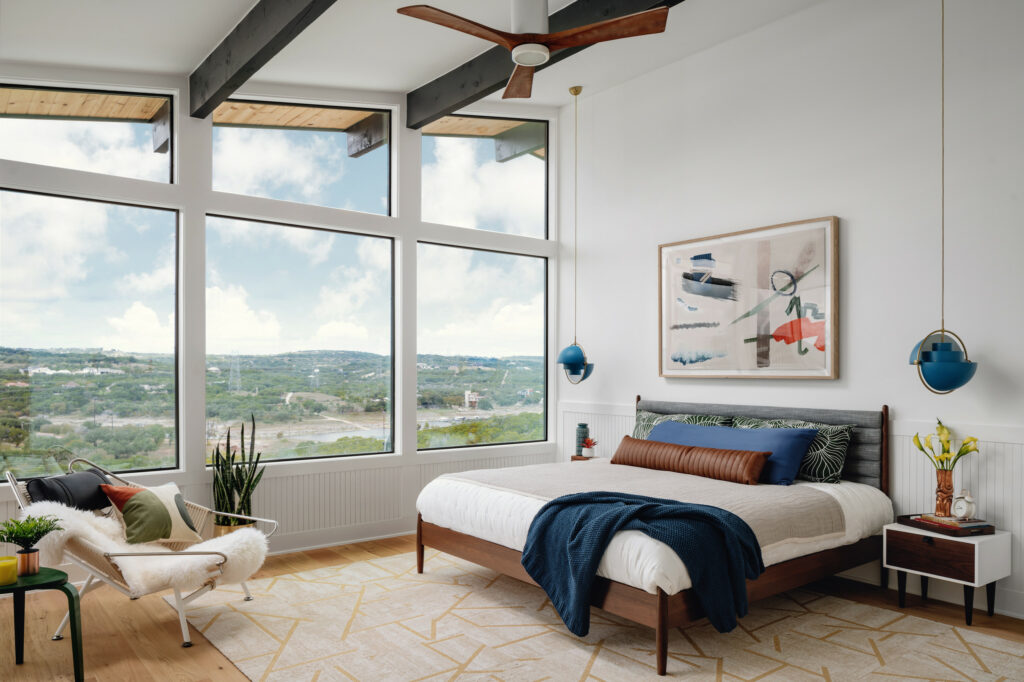 Bright bedroom with panoramic mountain views, mid-century furniture, and blue accents featuring wooden ceiling beams